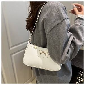 Detail of creamy white baguette bag with gold bow accent and pebbled leather texture