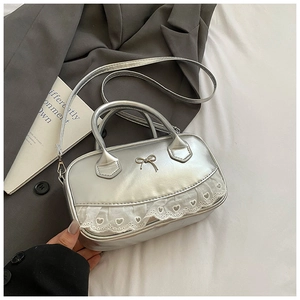 Dettaglio della mini borsa argento con pizzo e fiocco su biancheria da letto bianca