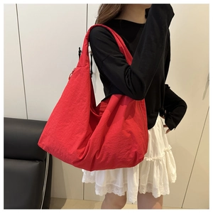 Close-up of a large red nylon tote bag with a wide shoulder strap on a female model