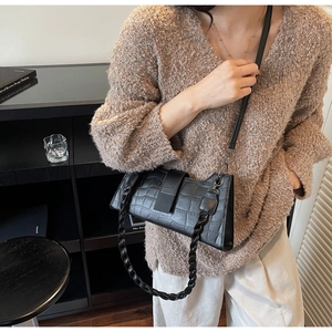 Close-up of black crocodile-embossed baguette bag with woven chain and leather strap