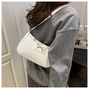 Detail view of white shoulder bag featuring gold bow hardware and pebbled leather texture