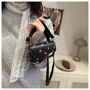 Close-up of mini black crossbody bag with cherry prints and golden metal buckle detail