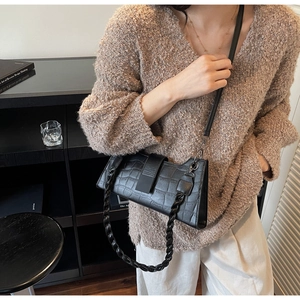 Detail of black crocodile pattern baguette bag with wide woven strap and metal buckle