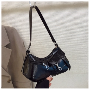 Detailed close-up of glossy black shoulder bag with metal hook and pocket texture