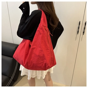 Detail view of large red nylon hobo bag with a modern triangular silhouette on shoulder