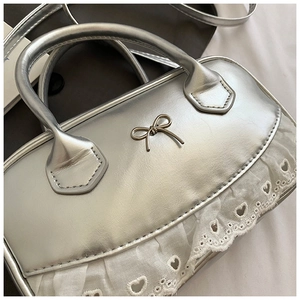Dettaglio ravvicinato della borsa in pelle argento con fiocco in metallo e pizzo