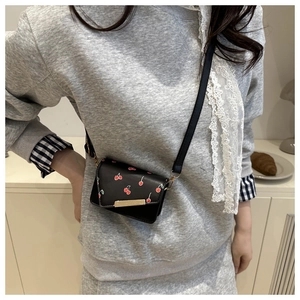 Detailed view of black mini crossbody bag with cherry prints and golden metal trim decor