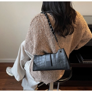 Close-up of black crocodile pattern baguette bag with stylish twisted woven shoulder strap