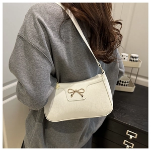 Close-up of a white leather baguette bag with a golden bow and lychee texture