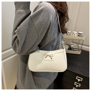 Detail of white litchi leather baguette bag with golden bow and flower pendant