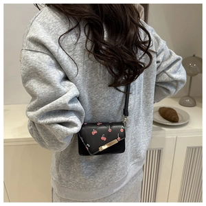 Close-up of black crossbody bag featuring cherry prints and a golden metal clasp detail
