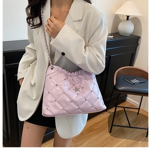 Detail of lavender quilted bucket bag with star charms and chain strap on a white blazer
