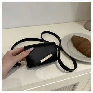 Close-up of a mini black glossy crossbody bag with gold metallic bar detail in hand