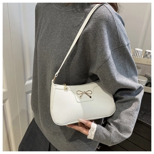 Close-up of a white lychee leather baguette bag featuring a gold bow buckle detail
