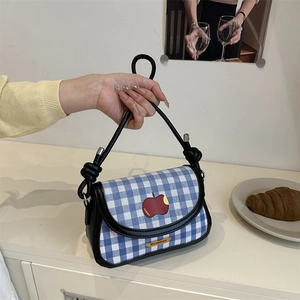 Detail of blue vichy plaid handbag with red apple patch and black rope knot handle