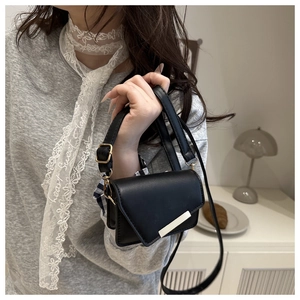 Detailed view of the black mini crossbody bag featuring a sleek metal bar flap closure