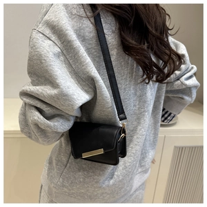 Detail shot of a black mini crossbody bag with gold metal hardware worn by a model