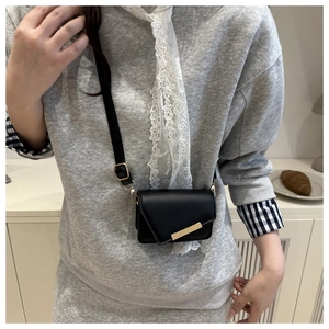 Detailed shot of a black mini crossbody bag with gold metal buckle on a grey sweater