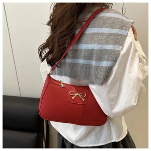 Detail of red faux leather shoulder bag with gold bow buckle and flower charm