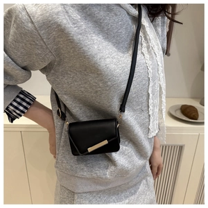 Detail view of a black mini crossbody bag with gold bar accent worn by a model