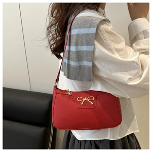 Red pebbled leather baguette bag with golden bow worn by a model in soft light