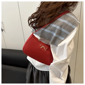 Detailed side view of a red baguette shoulder bag with a gold bow buckle on model