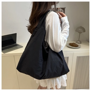 Detailed side view of the black canvas tote bag worn by a model in a minimalist setting