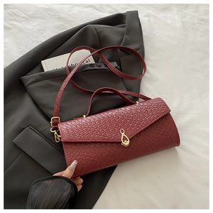 Dettaglio borsa rossa intrecciata con chiusura dorata su sfondo di blazer grigio