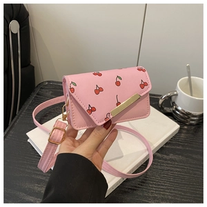 Detailed close-up of pink cherry print crossbody bag with gold buckle on wooden table