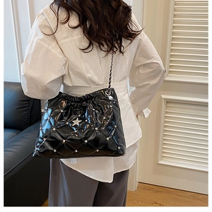Side view of black quilted bucket bag with star rivets and chain strap on shoulder