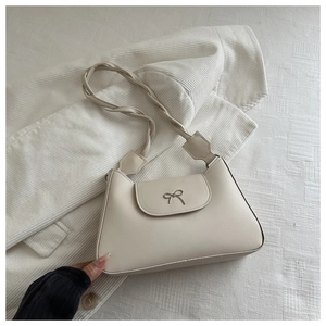 Close-up of cream underarm bag with metal bow detail and woven twist shoulder strap