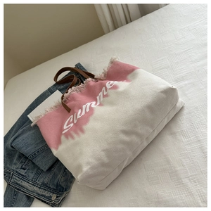 Detail of pink canvas beach tote with frayed edges and brown leather handles on bed