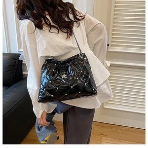 Detail of black quilted patent leather bucket bag with crystal star and chain strap