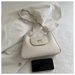 Detail of cream shoulder bag featuring metal bow buckle and braided rope strap design