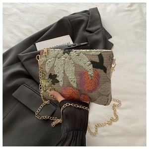 Détails de broderies florales et paillettes sur une pochette en tissu beige
