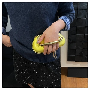 Detail of a bright yellow clutch bag featuring a thick gold U-shaped metal handle