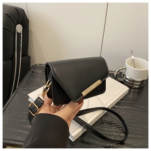 Detail of a black crossbody bag showing the asymmetrical flap and gold metal bar accent
