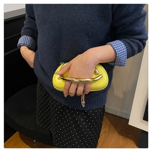 Détail d'une pochette jaune vif avec une poignée métallique sculpturale en forme de U