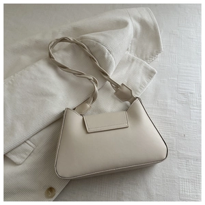 Close-up of beige underarm bag featuring a unique braided shoulder strap on soft fabric