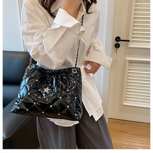 Detail of black quilted shoulder bag with silver star studs and chain strap shown on model