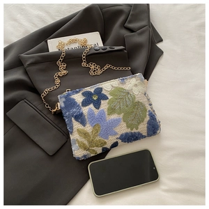 Détail de la broderie complexe de fleurs à paillettes et chaîne dorée sur le sac de soir