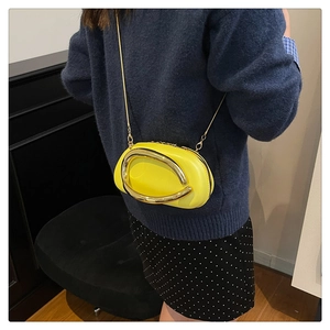 Detail of a bright yellow oval crossbody bag with large gold metal ring and thin chain strap