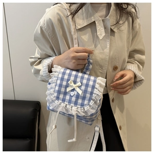 Detail of blue plaid mini bag with white lace trim, heart button, and bow decoration