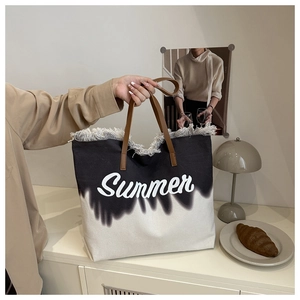 Detail of gradient canvas tote with fringe trim and leather handles in a cozy setting