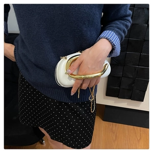 Detail of white leather handbag featuring chunky gold metal handle and chain strap