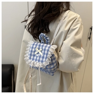 Close-up of blue plaid backpack with white lace trim, ruffles and a small bow detail