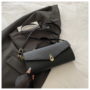 Dettaglio borsa nera a trama intrecciata con fibbia dorata su sfondo blazer grigio