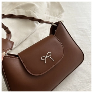 Close-up of retro brown shoulder bag with silver bow buckle and twisted woven strap detail