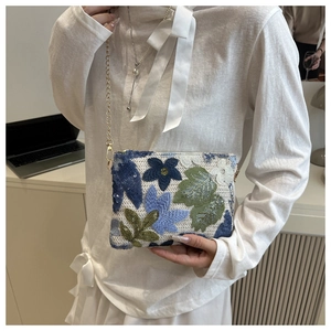 Détail d'un sac à main élégant à paillettes avec motifs floraux bleus et chaîne dorée