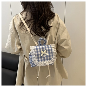 Detailed view of blue plaid backpack featuring white lace ruffles and yellow bow decoration